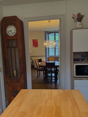 Un coin repas avec une table et des chaises en bois, une grande horloge murale et un luminaire suspendu.