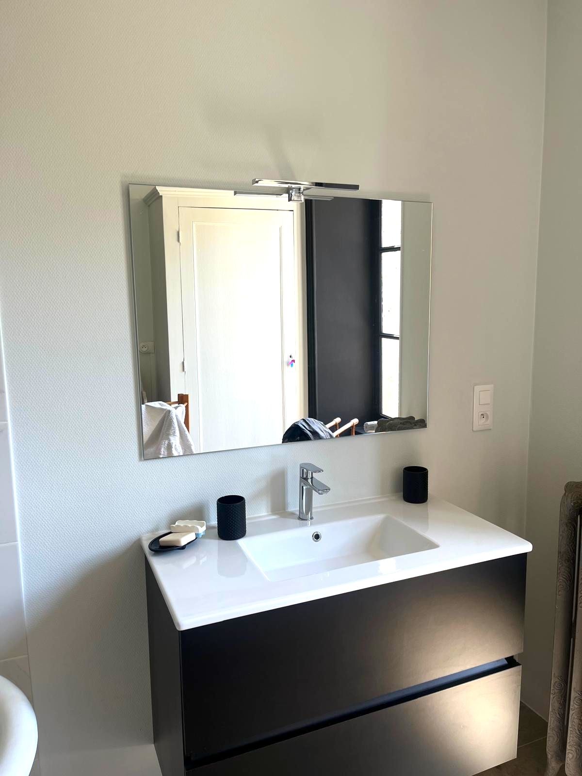 A modern bathroom with a white sink, a large mirror, and a black cabinet.