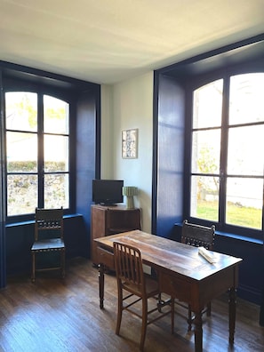 A room with a wooden table and chairs, a television on a stand, and large windows with a view of the outdoors. - Maison Dellac – Les clés du temps (Saint-Saturnin)