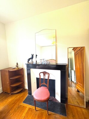 Ein Zimmer mit Holzboden, Kamin in Schwarz, ein roter Sessel, ein Holzschrank und ein Spiegel.