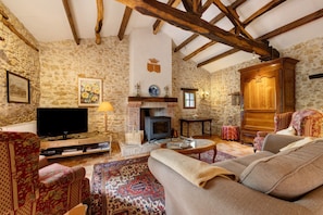 A rustic living room with stone walls, a fireplace, a television, and traditional furniture. - Le Gîte Du Château De La Vérie: terrace, private garden and Wi-Fi (Challans)