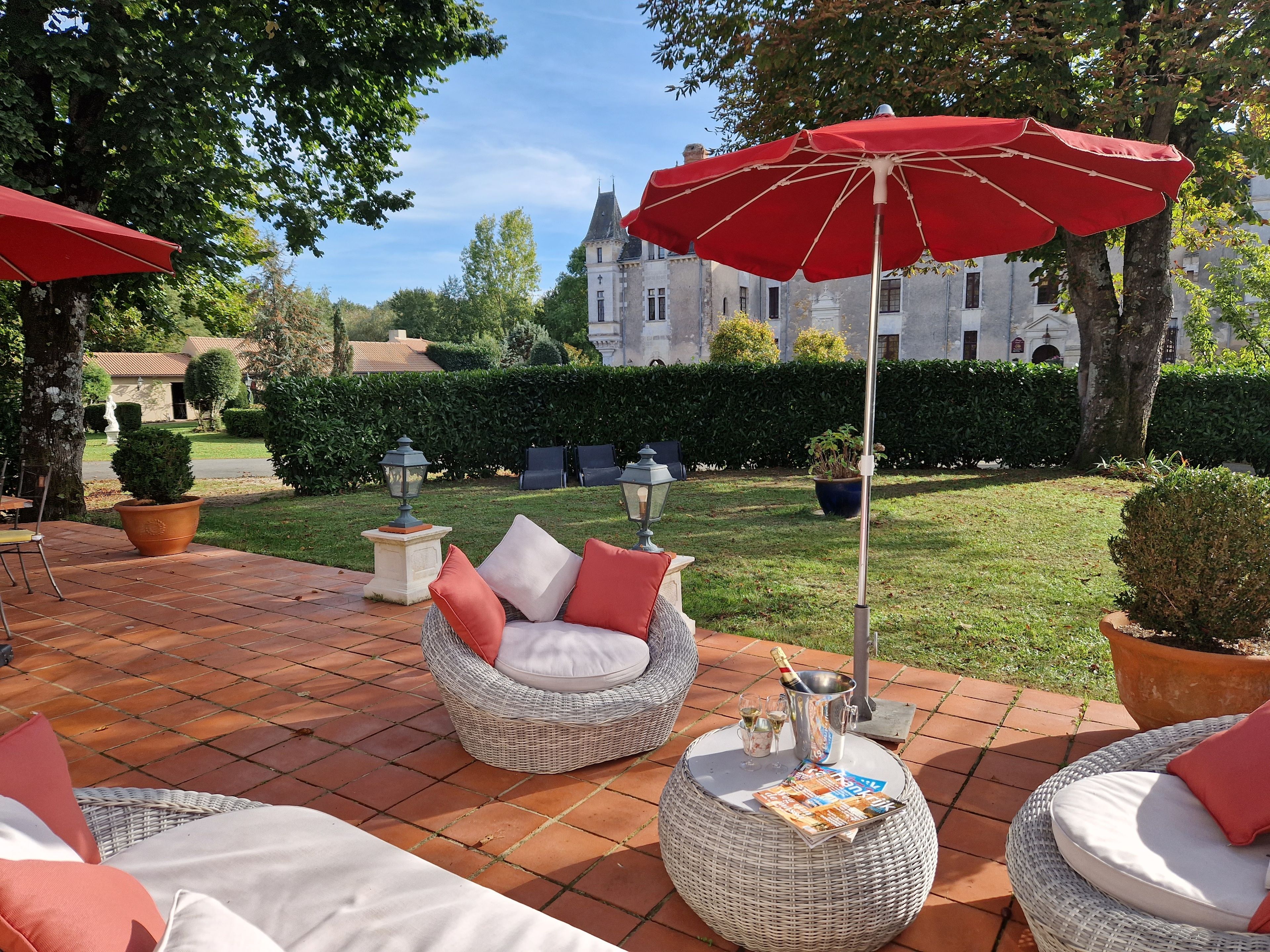 Un patio con mobiliario de mimbre, sombrillas rojas y una vista de un castillo al fondo.
