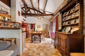 A rustic interior with exposed wooden beams, a tiled floor, a dining area with a table and chairs, and shelves with various items. - Le Gîte Du Château De La Vérie: terrace, private garden and Wi-Fi (Challans)