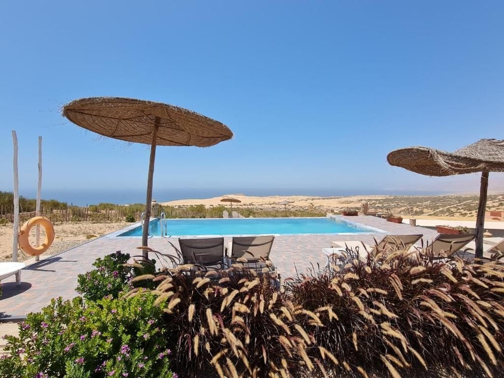 Área de piscina com espreguiçadeiras e guarda-sóis, emoldurada por paisagem desértica.