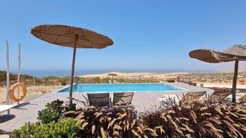 Área de piscina com espreguiçadeiras e guarda-sóis, emoldurada por paisagem desértica.
