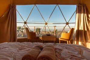 Una habitación con cama, dos sillas, una mesita y vistas del paisaje a través de un diseño de ventana geométrico.
