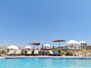 Zona de piscina amb gandules, ombrel·les i estructures de forma arrodonida.