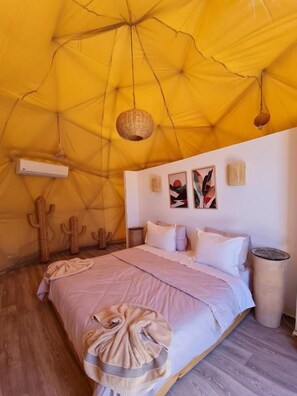 A room with a large yellow tent ceiling, a bed with white linens, and a cactus wall decoration.
