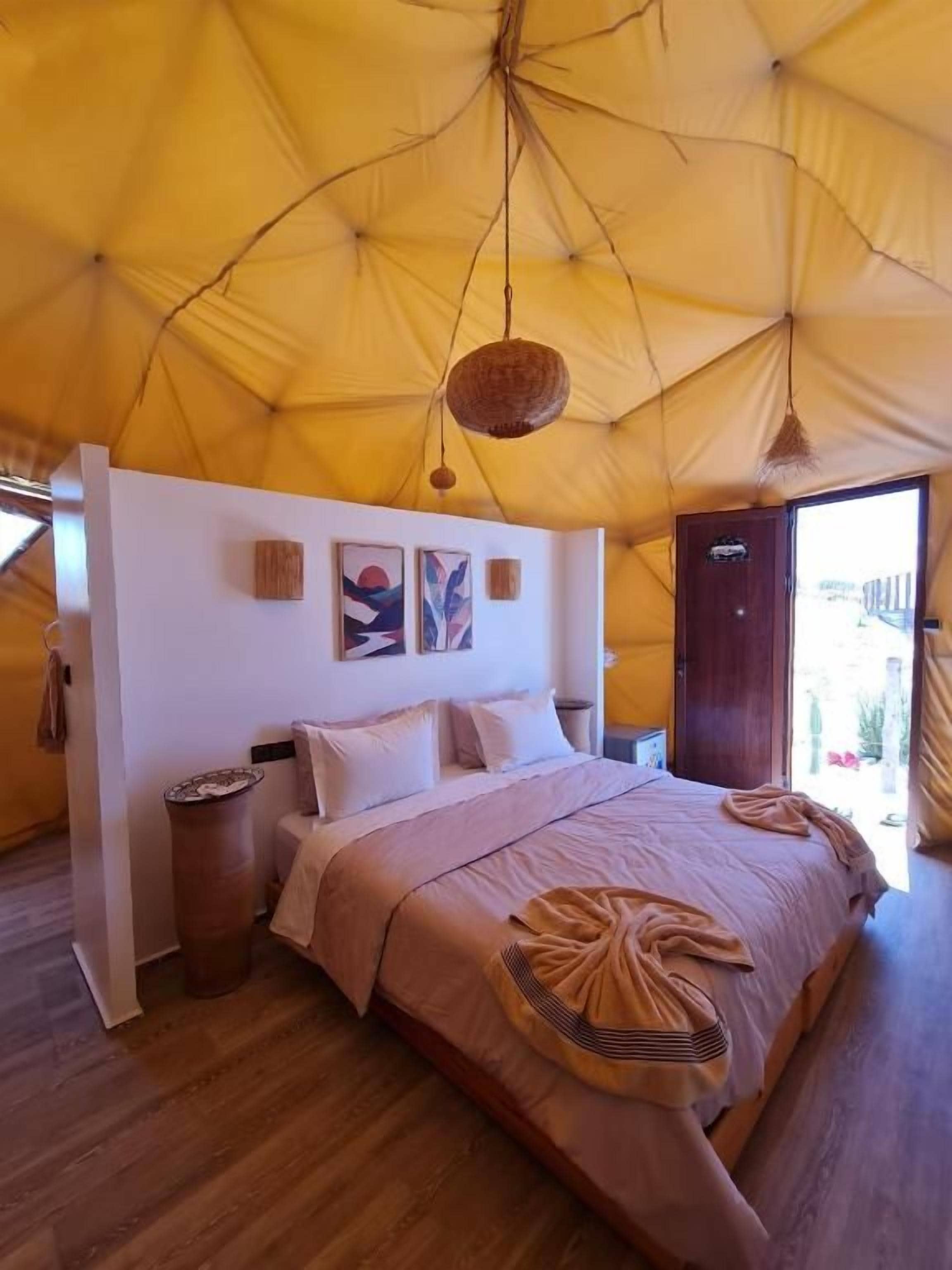 Un dormitorio con una cama grande, suelo de madera y una estructura de techo similar a una tienda de campaña.