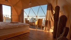 A tent-style room with a bed, chairs, and a view of the landscape.