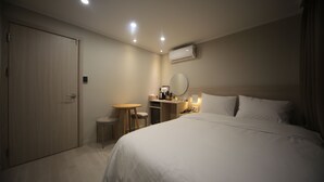 A hotel room with a bed, a desk, a chair, a small table, an air conditioning unit, and a door. - Hotel Picasso (Seoul)
