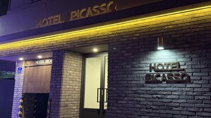Ein Hotel Eingang mit einem Schild, das 'HOTEL PICASSO' zeigt, und einer Ziegel-Fassade.