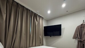 A modern bedroom with a large bed, a flat-screen TV mounted on the wall, and a robe hanging on a hook.