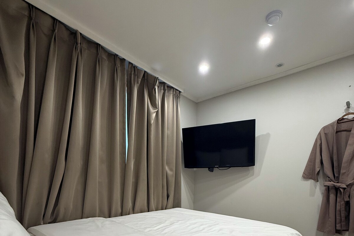 A modern bedroom with a large bed, a flat-screen TV mounted on the wall, and a robe hanging on a hook.