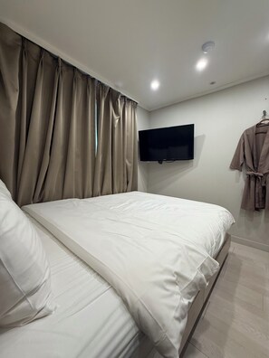 Une chambre moderne avec un grand lit, un téléviseur à écran plat fixé au mur et un peignoir suspendu à un crochet.