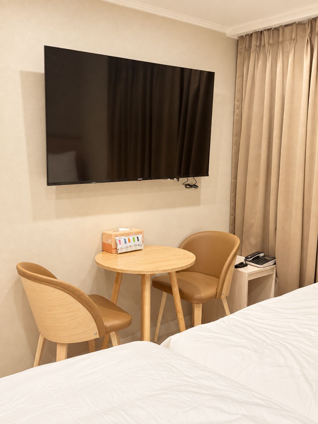 A hotel room with a bed, a TV mounted on the wall, two chairs, a small table, and a telephone.