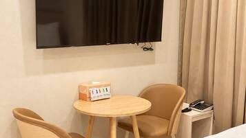 A hotel room with a bed, a TV mounted on the wall, two chairs, a small table, and a telephone.