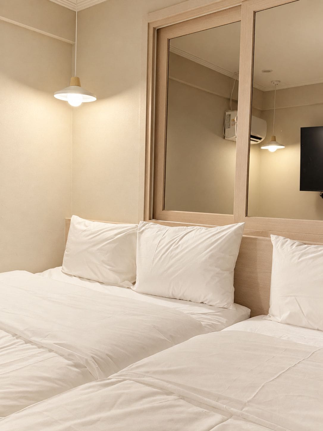 Habitación de hotel con cama, dos almohadas, un espejo y televisor montado en la pared.