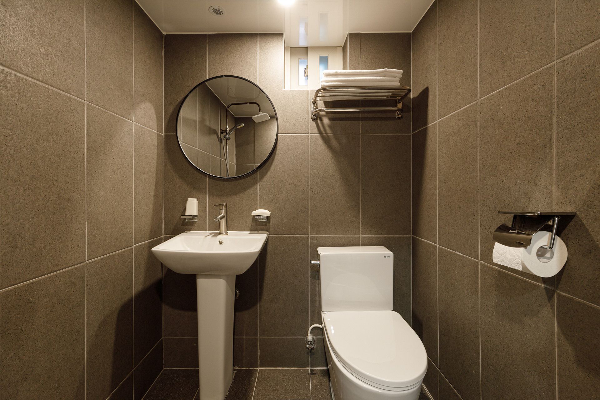Ein modernes Badezimmer mit Waschbecken, Toilette und einem runden Spiegel.