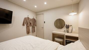 A hotel room with a bed, a TV, a mirror, a hairdryer, and robes hanging on the wall.