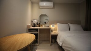 Quarto de hotel com cama, escrivaninha com espelho, espelho redondo, mesa e ar condicionado.