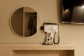 A bathroom with a round mirror, a hairdryer, and a wooden vanity. - Hotel Picasso (Seoul)