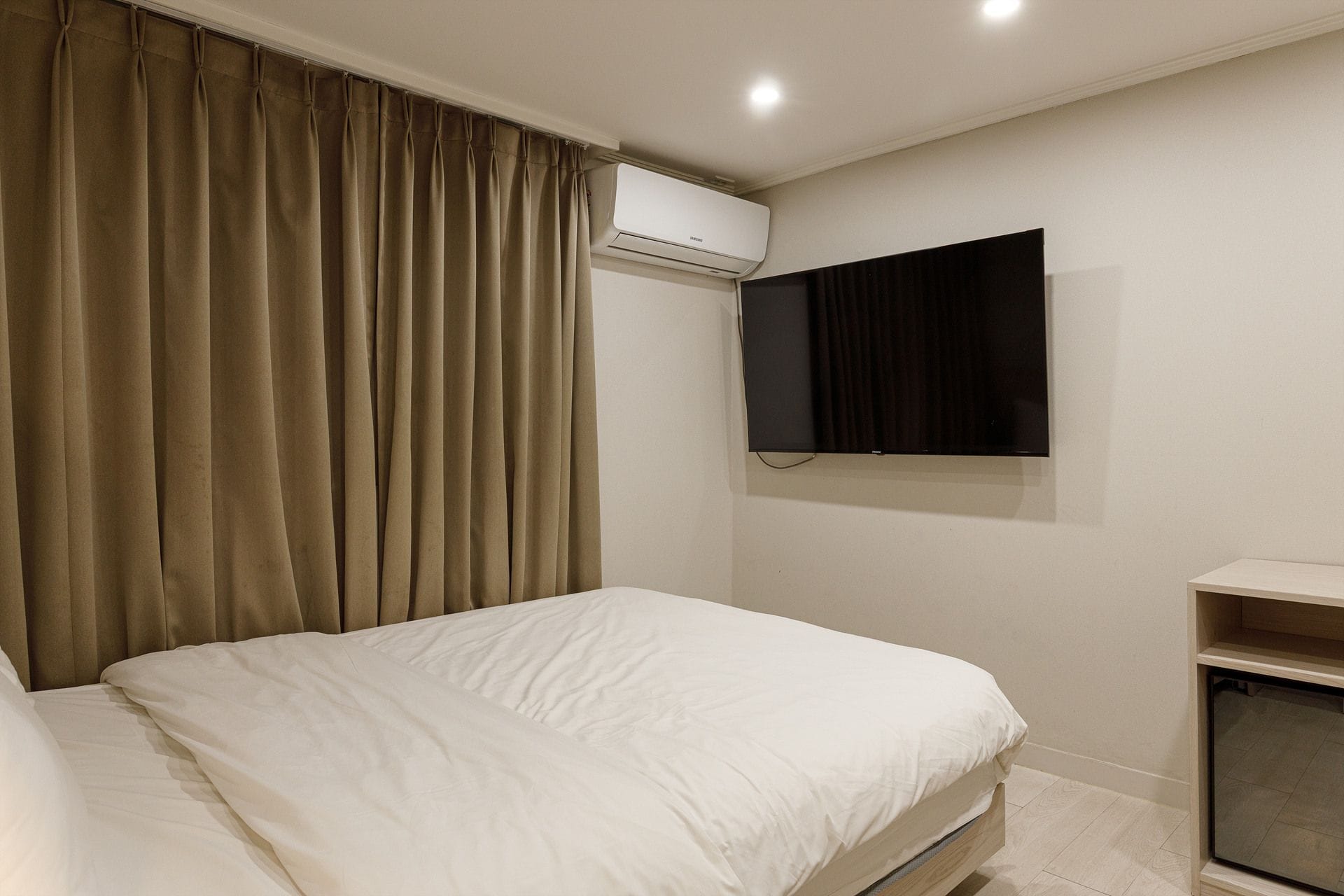 A bedroom with a bed, an air conditioning unit, a television, and a small cabinet.