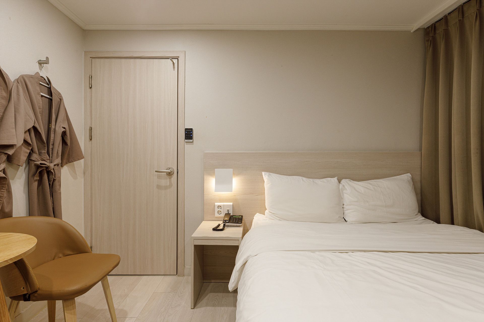 Una habitación de hotel con una cama, mesita de noche, silla y una puerta con perchero.