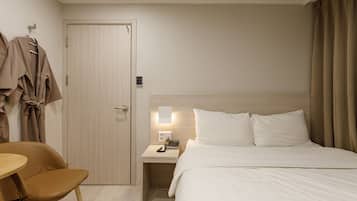 Una habitación de hotel con una cama, mesita de noche, silla y una puerta con perchero.