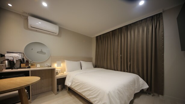 A hotel room with a bed, bedside table, desk with a computer, and an air conditioning unit. - Hotel Picasso (Seoul)
