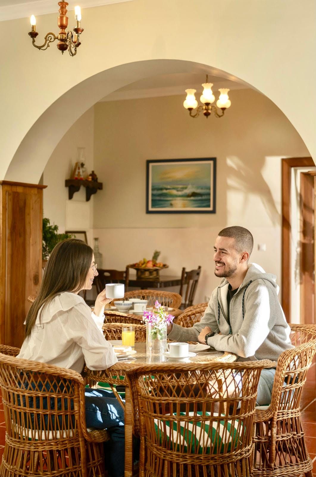 A dining area with wicker chairs, a table with breakfast items, and a painting on the wall.