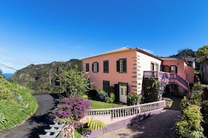 A pink villa with a curved driveway, a staircase, and a view of the surrounding greenery and hills. - Villa da Fajã Alta - Room No. 4 (Santana)