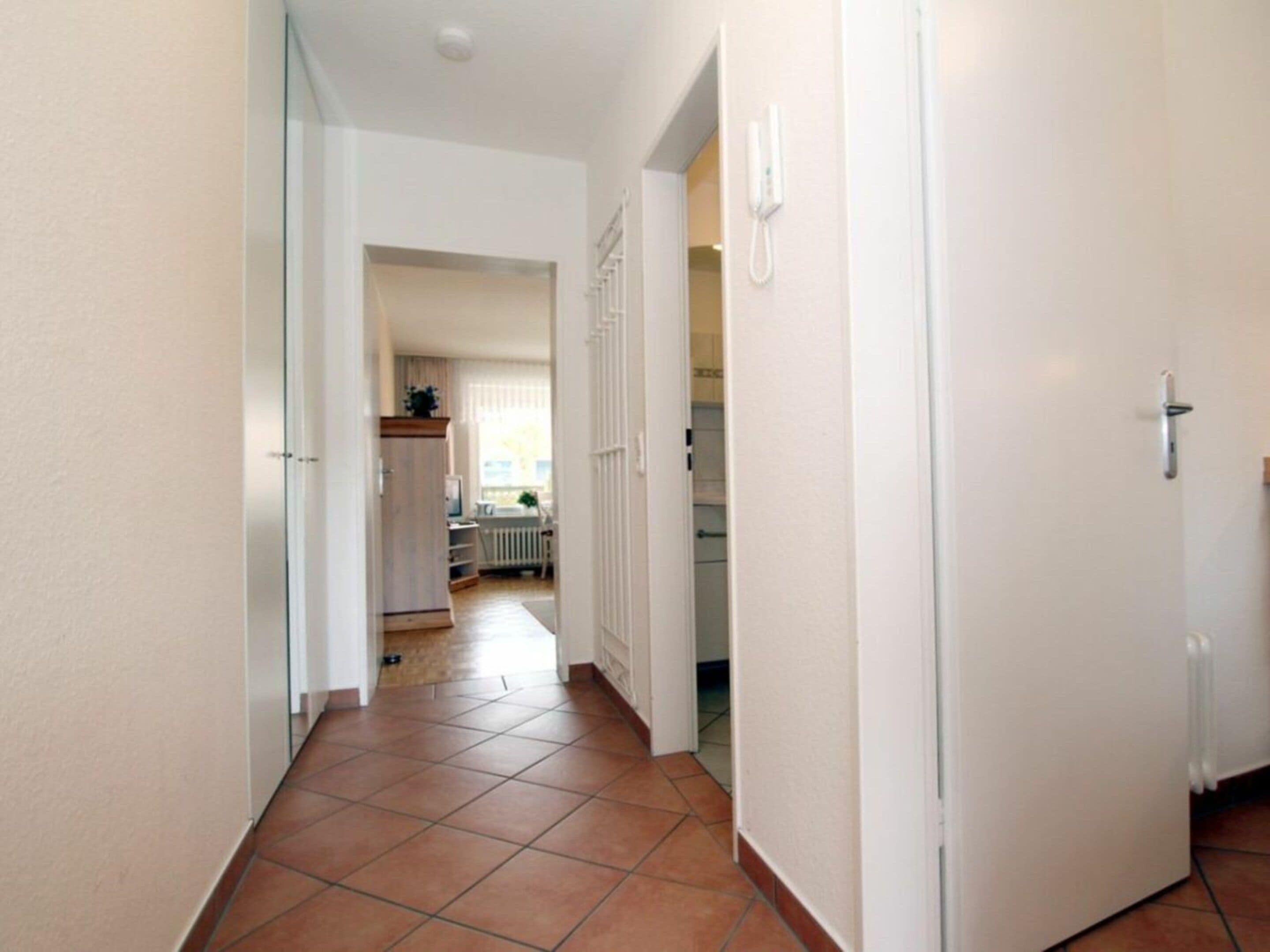 A corridor with a tiled floor leading to a room with a radiator and a window.
