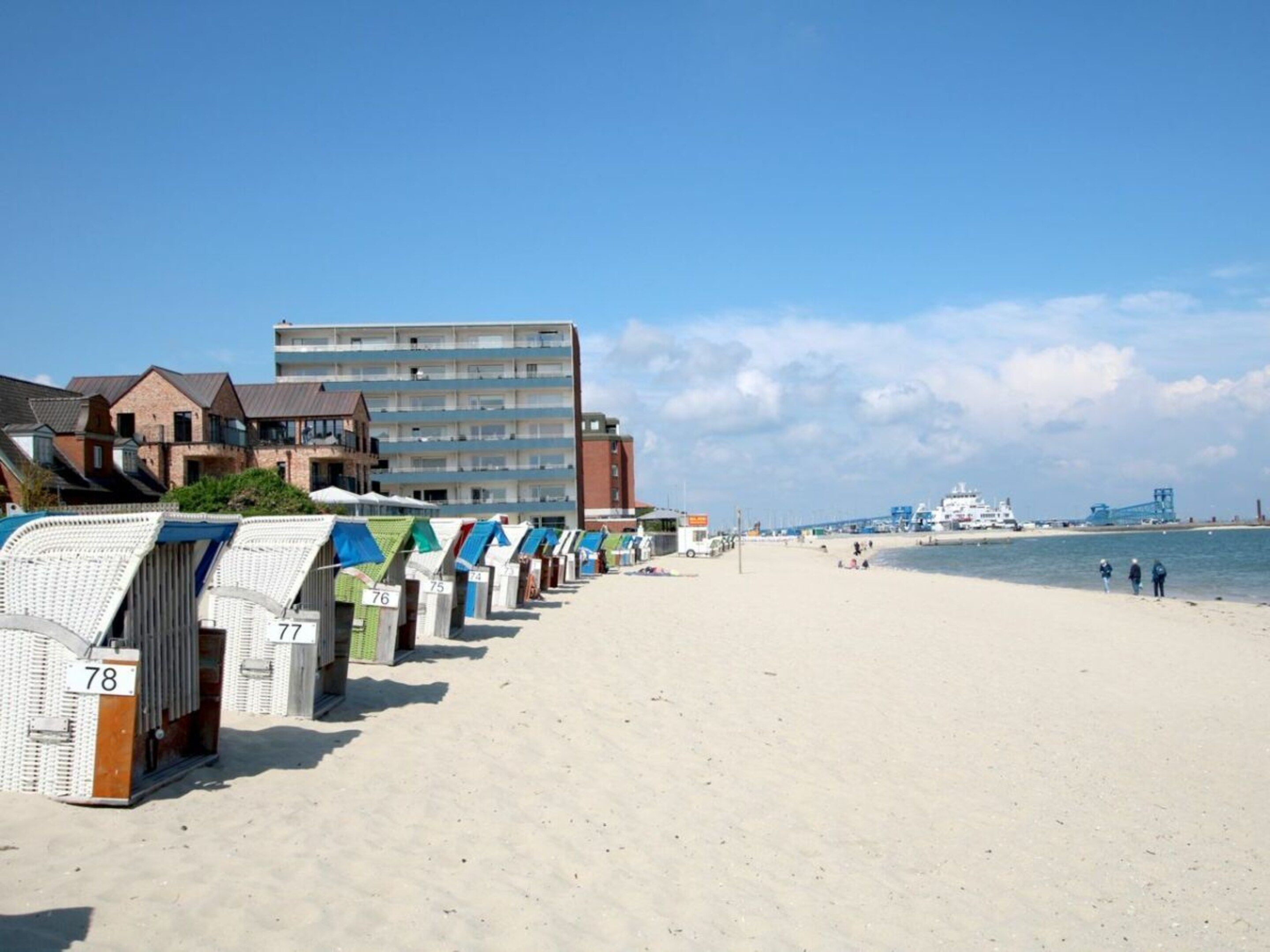 A beach with numbered beach huts and a building in the background.