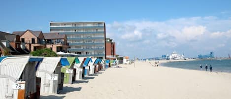 A beach with numbered beach huts and a building in the background.