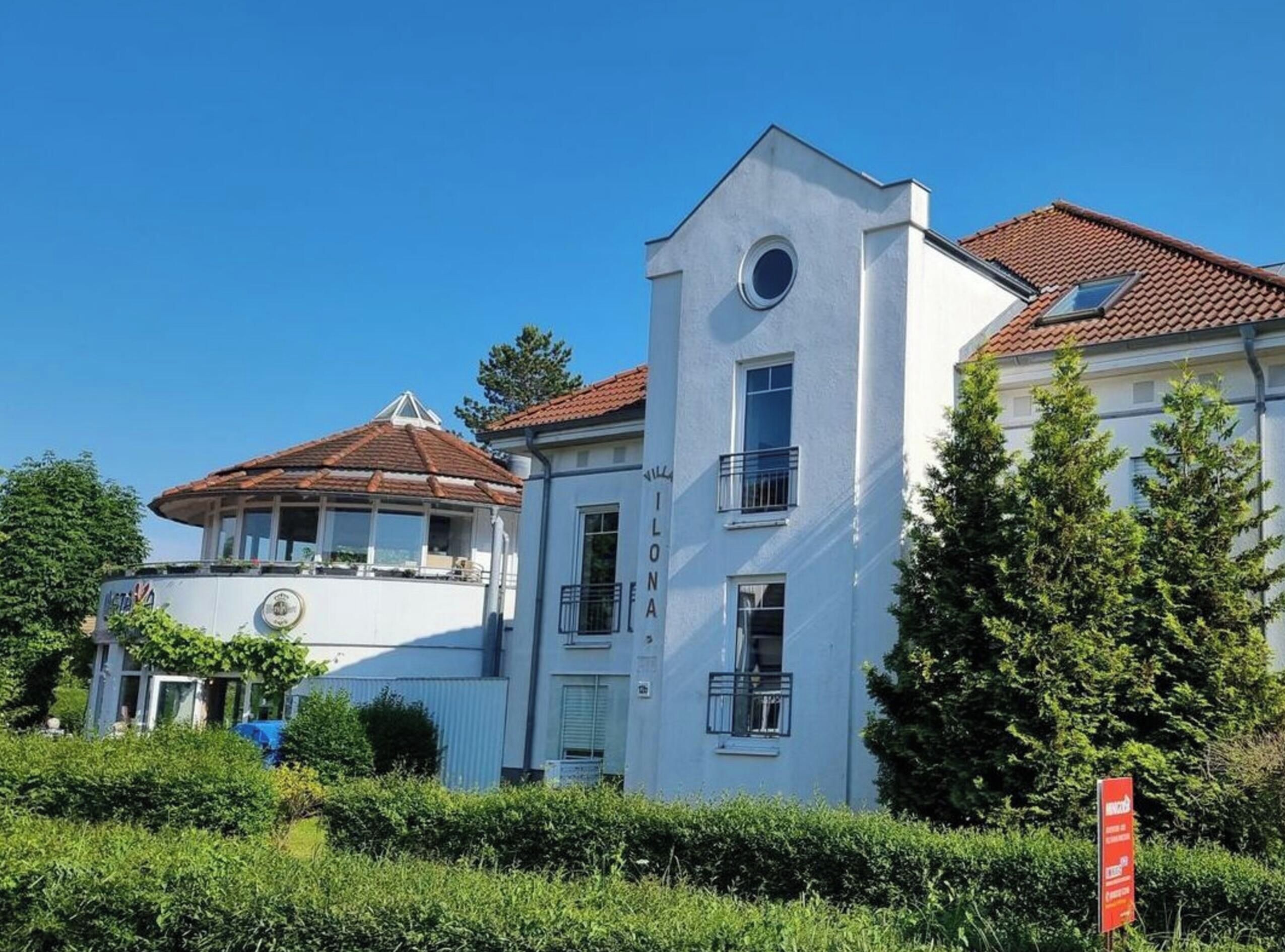 Un bâtiment à deux étages, doté d’une façade blanche, d’un toit recouvert de tuiles rouges et d’une fenêtre circulaire au deuxième étage.