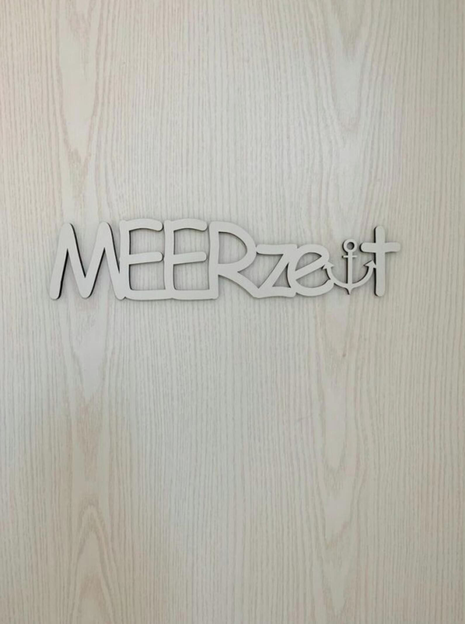 Pared de madera con la palabra 'MEERzeit' recortada en una tipografía estilizada.