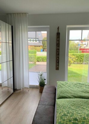 Ein Zimmer mit einer Couch, einer Topfpflanze und Blick auf einen Garten durch ein Fenster.