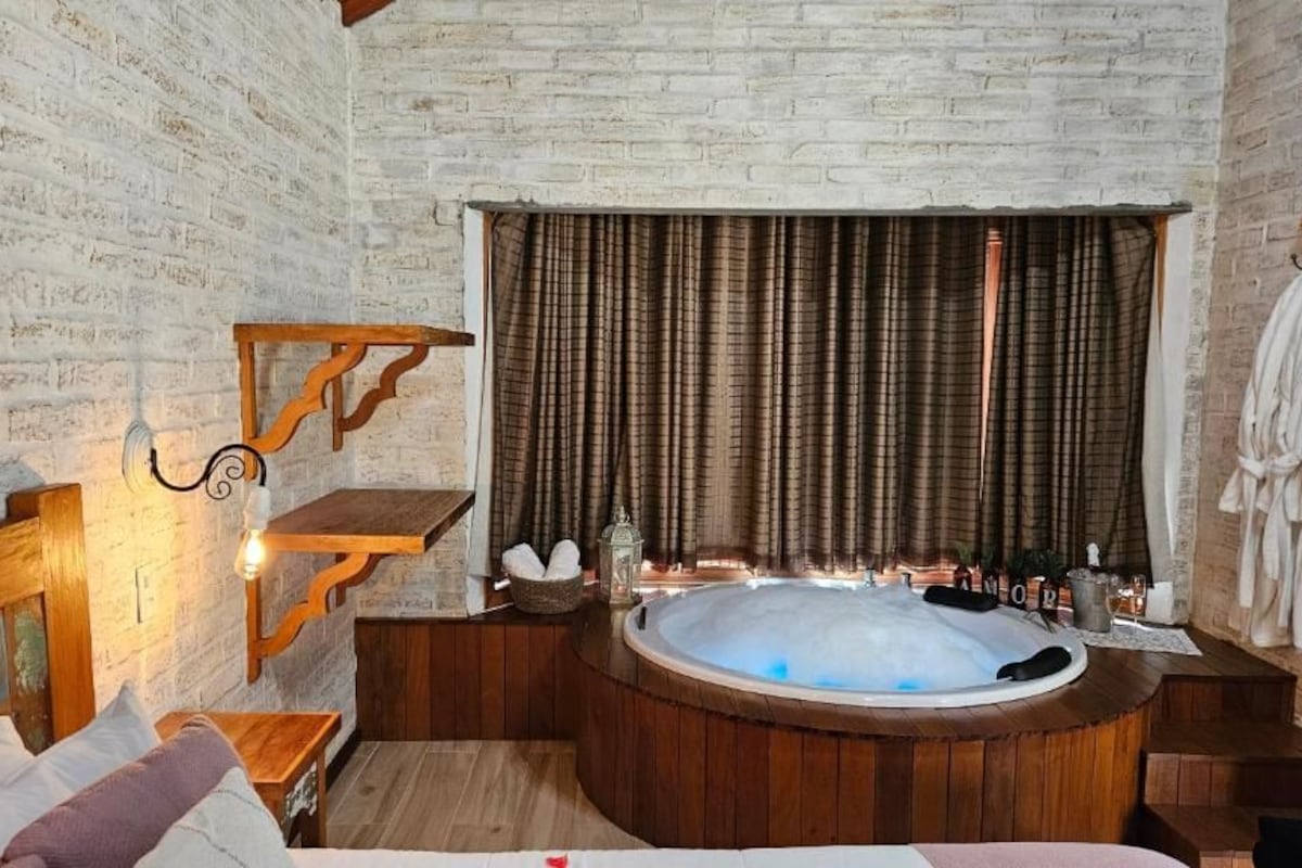 Ein Zimmer mit einer großen Holzwanne, einer Holzbank, einem kleinen Tisch und einem an der Wand befestigten Regal.