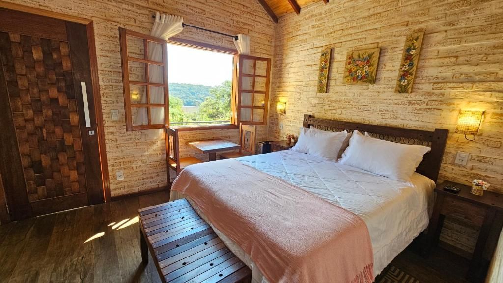 A bedroom with a wooden bed, a bench, a window with a view, and a brick wall.