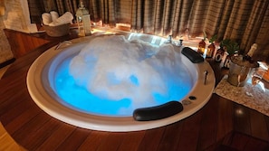 Ein Whirlpool mit blauem Licht, umgeben von Holzboden, einer Steinwand sowie verschiedenen Flaschen und Pflanzen.
