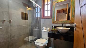 A bathroom with a glass-enclosed shower, a toilet, and a sink with a mirror above it.