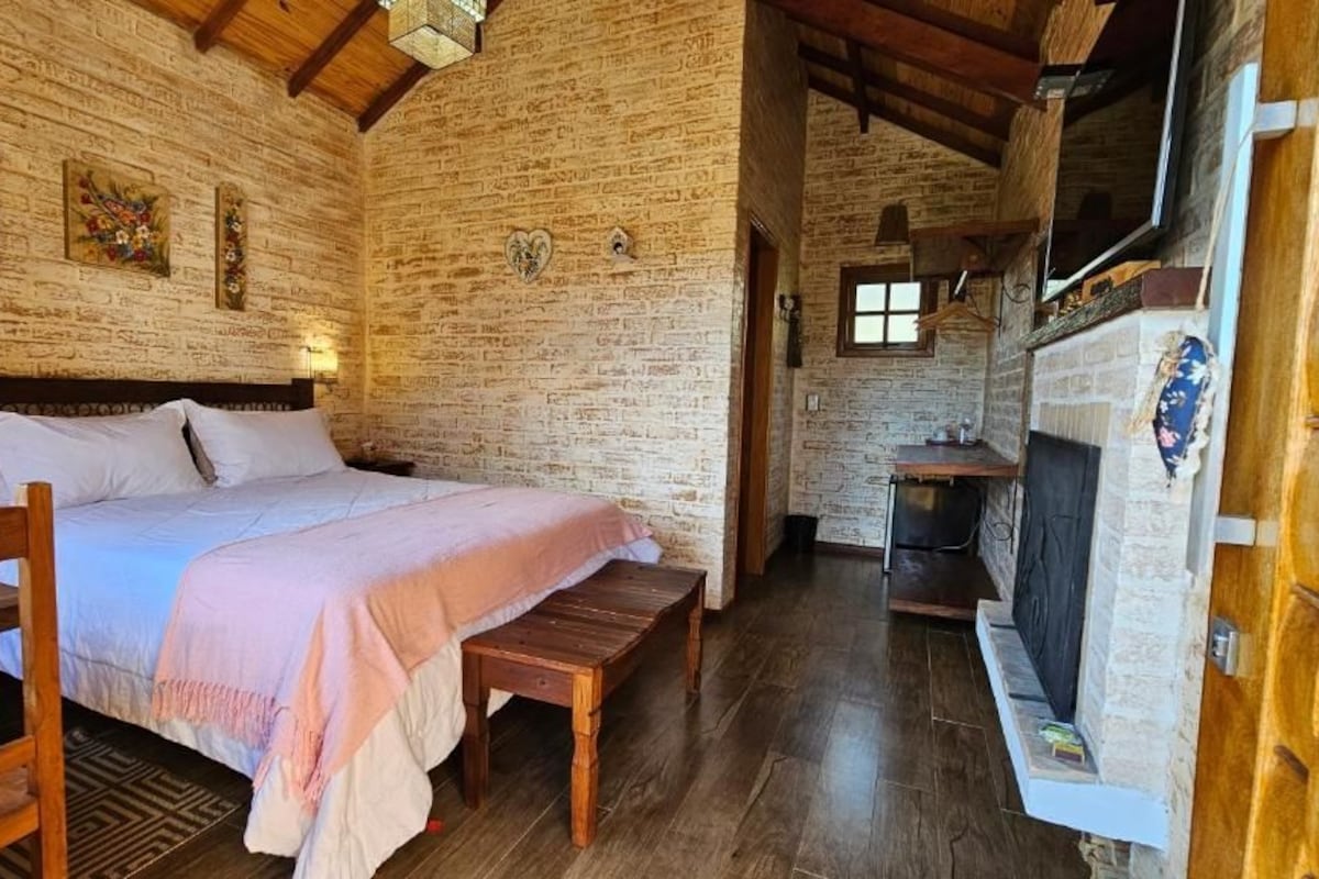 Una habitació amb un llit, una panxa de fusta, parets de maó i una llar de foc.