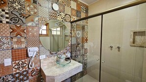 Un baño con pared de azulejos, cabina de ducha con mampara de vidrio, lavabo con recipiente de cristal y un teléfono.