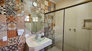 Un bany amb una paret revestida de rajoles, una cabina de dutxa de vidre, un lavabo amb una pica de vidre i un telèfon.