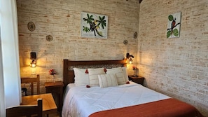 Ein Zimmer mit einer Ziegelwand, einem Bett mit weißer Bettwäsche, zwei Nachttischen mit Lampen und einem Kunstwerk mit Vogelmotiven.