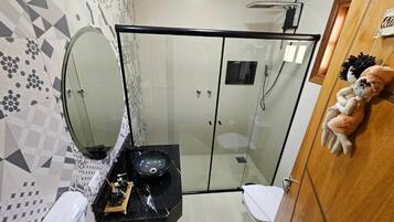 A bathroom with a glass shower enclosure, a toilet, a sink with a mirror, and a decorative item on the wall.