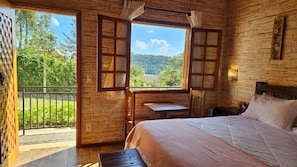 A bedroom with a bed, a small table, and a window with curtains. - Noma Monte Verde (Camanducaia)
