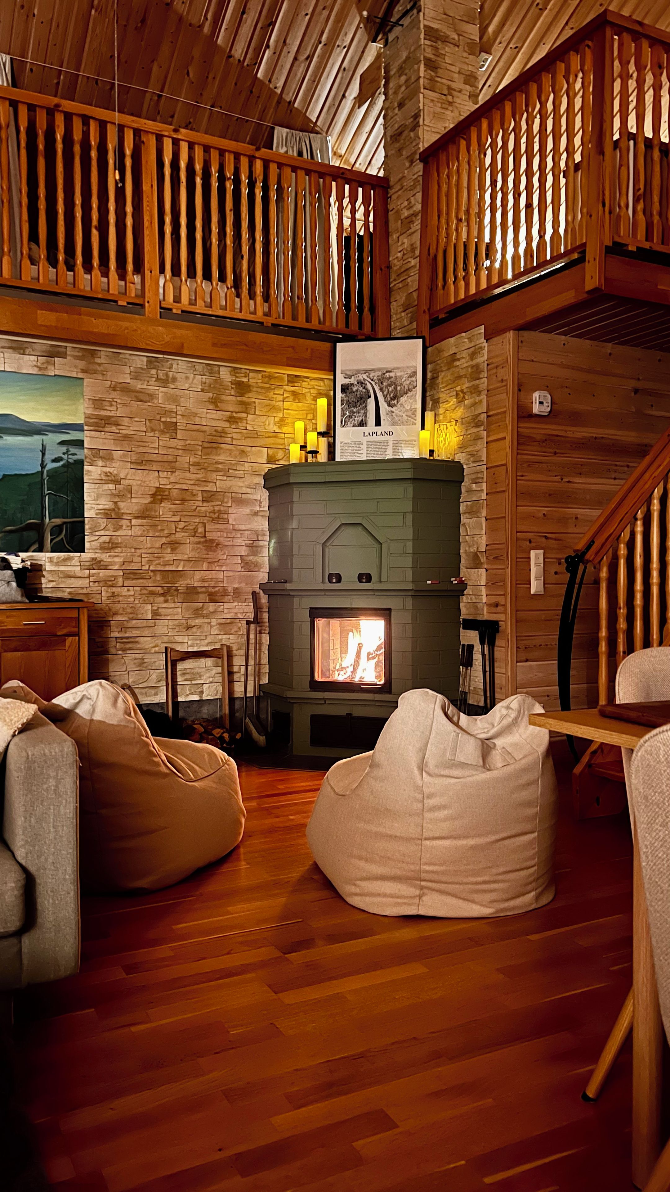 A cozy cabin interior with a fireplace, wooden walls, and a loft area.