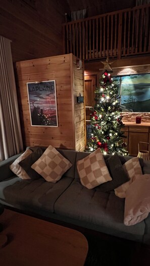 L’intérieur chaleureux d’un chalet avec un mur en bois, un sapin de Noël et un canapé agrémenté de coussins à motifs.